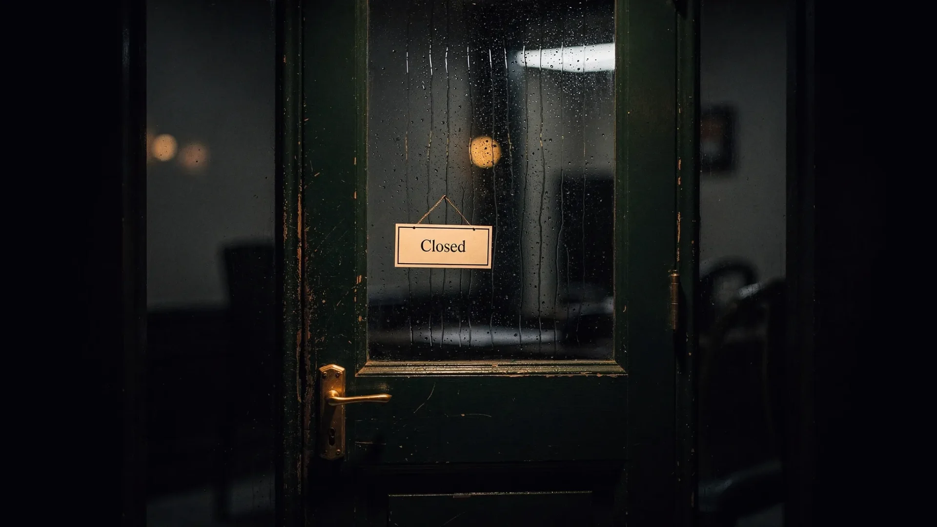 A cinematic, moody scene of a small office door with a simple “Closed” sign hanging, deep dark green tones with gold highlights, rain-streaked glass, no text beyond the sign, no people, high contrast lighting.