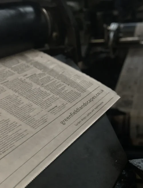 A local business’s web address appears in a newspaper article emerging from a printing press, a real-world example of one referring domain linking to a website.