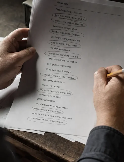 Hands sort printed search phrases beside a phone and notebook, showing the work of choosing useful long-tail keywords.